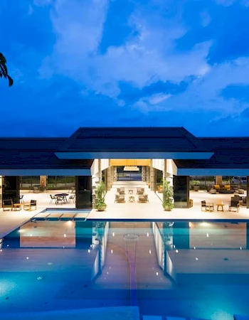 A luxurious contemporary building with a pool in front, illuminated in the evening with a dramatic blue sky backdrop.