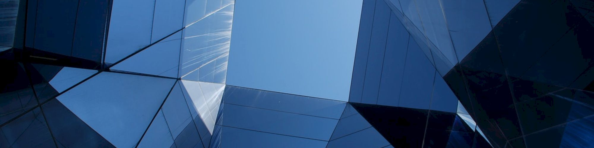 The image shows an abstract view of mirrored glass buildings reflecting the sky, creating a geometric pattern with a calm blue tone.