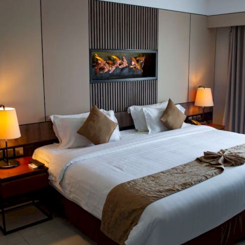 A cozy hotel room with a large bed, two bedside lamps, and a decorative piece above the bed, creating a warm and inviting atmosphere.
