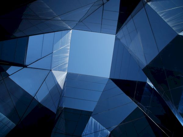 The image shows a geometric architectural structure with reflective glass panels, creating a symmetrical pattern against the sky.