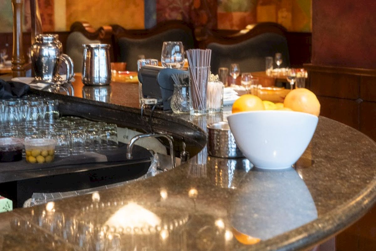 A bar counter with a bowl of citrus fruits, glasses, a pitcher, and various bar tools and accessories displayed neatly.