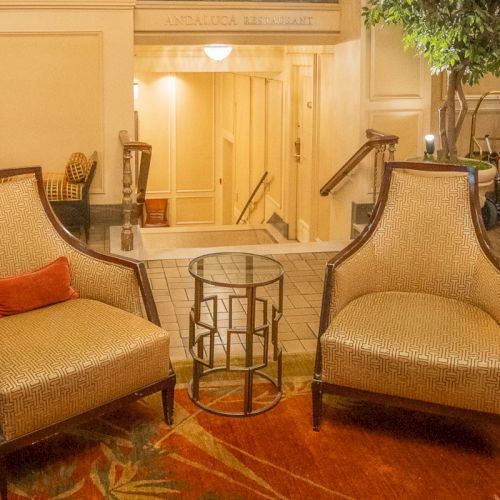 The image shows two chairs with a small glass table between them, placed on a rug, creating a cozy seating area in a warmly lit room.