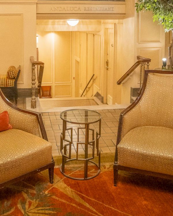 The image shows two chairs with a small glass table between them, placed on a rug, creating a cozy seating area in a warmly lit room.