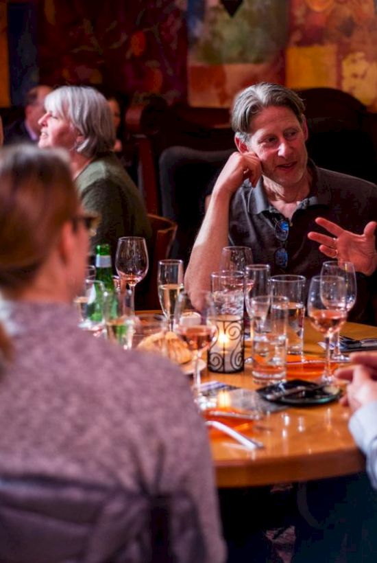 A group of people are sitting around a table in a restaurant, engaged in conversation, with drinks and glasses on the table.