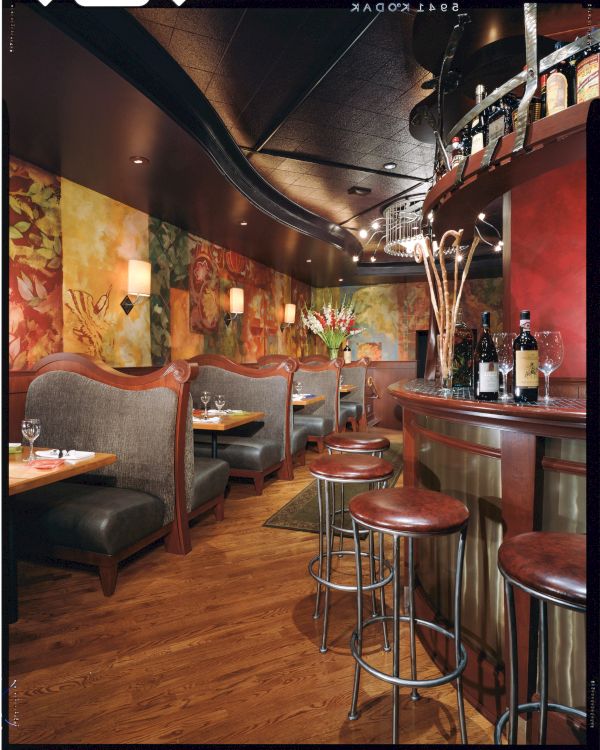 A cozy, upscale bar with curved leather booths, warm wood flooring, colorful mural walls, and a small counter with bar stools and drinks.