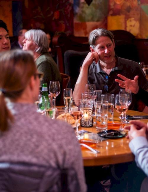 A group of people are sitting around a table in a restaurant, engaged in conversation, with drinks and glasses on the table.