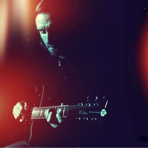 A person is playing an electric guitar in a dimly lit setting with colorful light effects in the background.