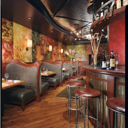 A cozy dimly lit bar with booth seating, colorful wall murals, a small counter with stools, and bottles on display, warm wood tones, intimate vibe.