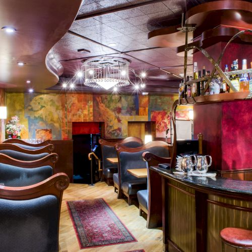A cozy, artful bar with curved leather booths, colorful mural walls, warm lighting, and a curved counter with stools, inviting and stylish.