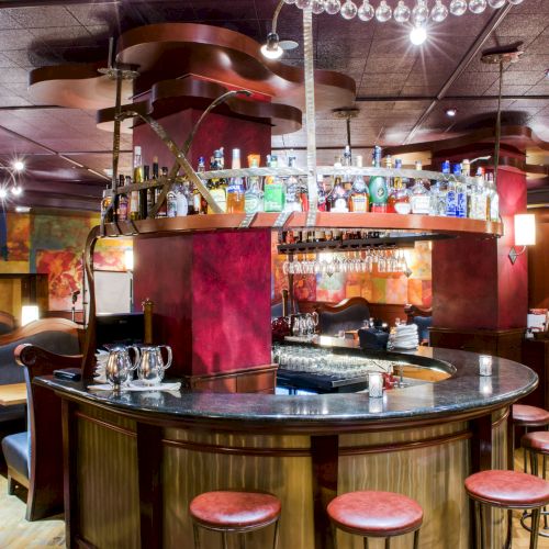 A round, retro‑style bar with stools, warm lighting, shelves of bottles, and a chef‑style counter, cozy dining booths, and colorful decor.