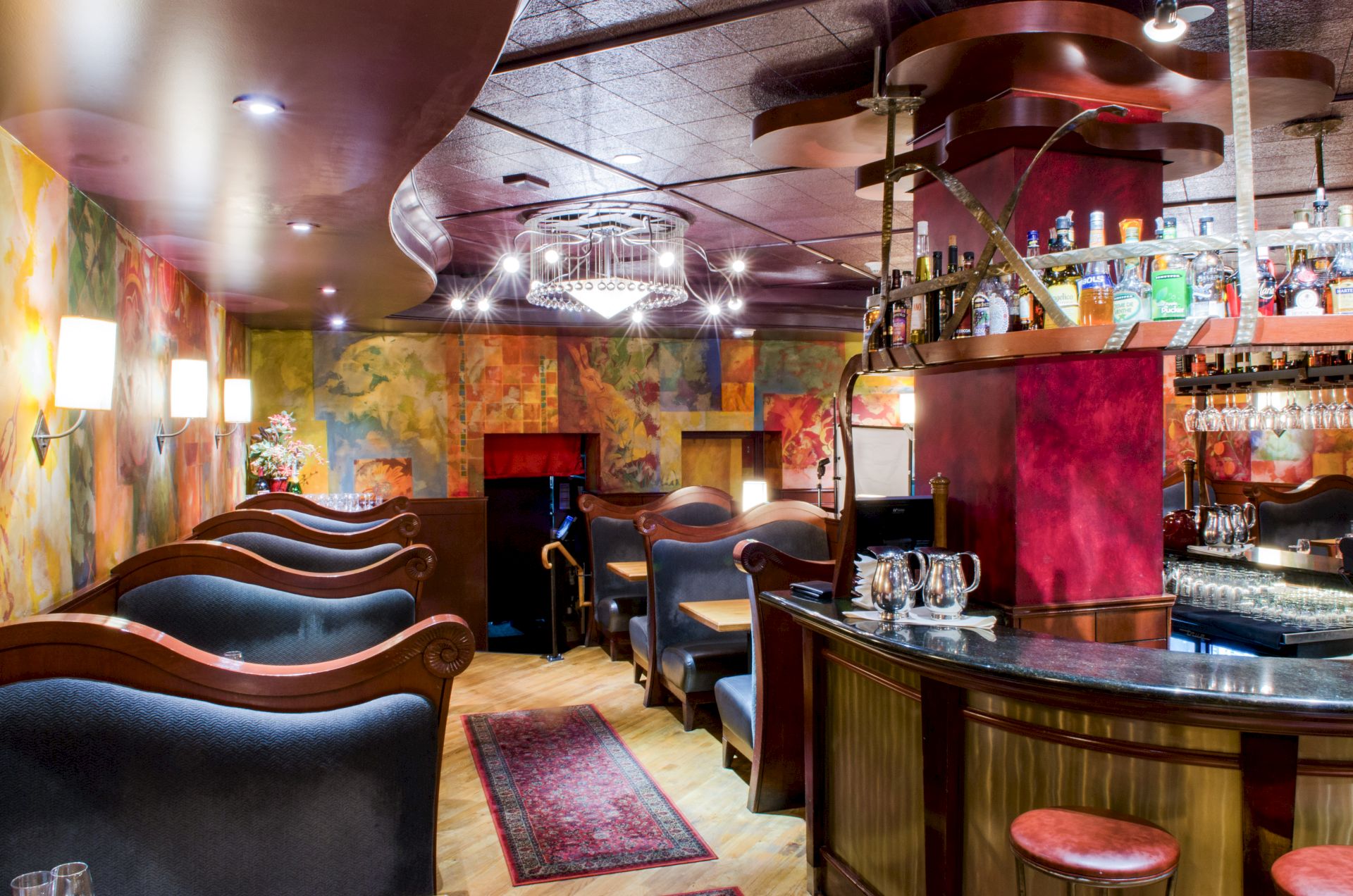 A stylish lounge or bar with curved seating, colorful mural walls, warm lighting, a curved counter, and a small bar area with stools, cozy and artistic.