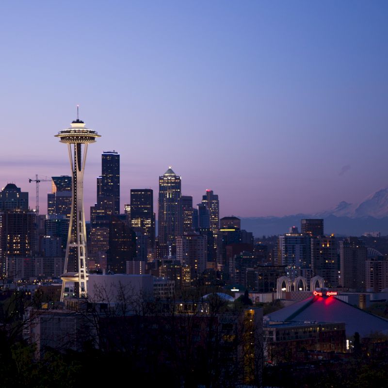 The image shows the Seattle skyline at dusk, featuring the Space Needle and Mount Rainier in the background.