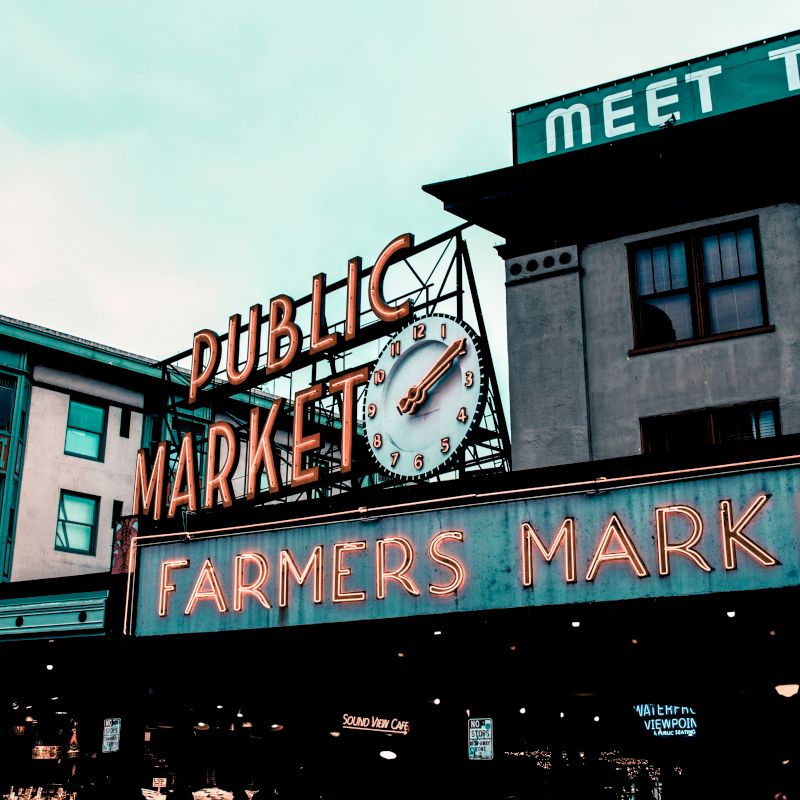 The image shows a neon sign for a "Public Market" and "Farmers Market" with a clock, likely an iconic location in a city.