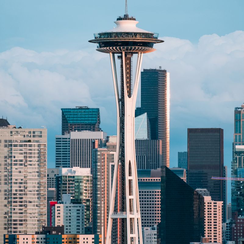 The image features the Space Needle against a backdrop of downtown skyscrapers in Seattle, with a cloudy sky.