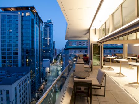 A modern rooftop terrace with seating overlooks a cityscape at dusk, featuring illuminated buildings and a tranquil ambiance.
