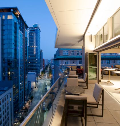 A modern rooftop terrace with seating overlooks a cityscape of tall buildings during twilight.