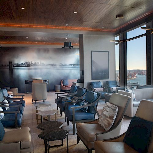 A modern lounge with comfortable seating, a panoramic wall art, and large windows offering a scenic view outside.
