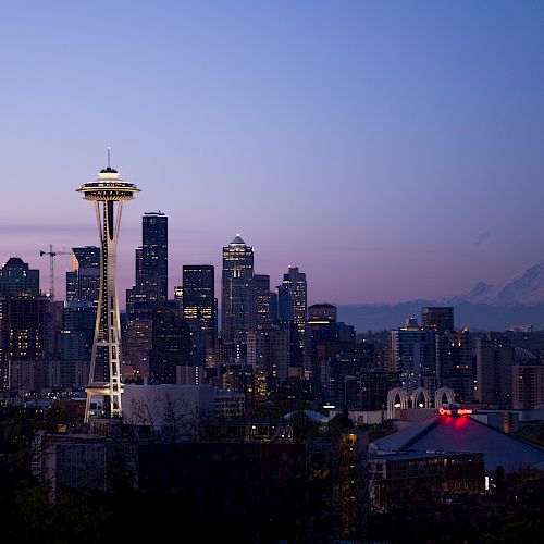 Seattle skyline at dusk with the Space Needle prominently visible, and Mount Rainier in the background.
