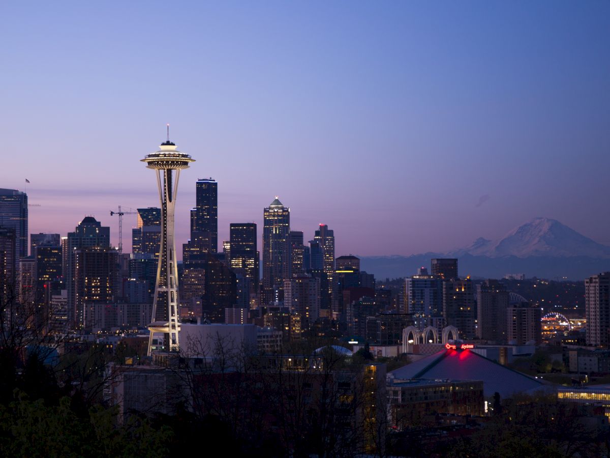 The image shows the Seattle skyline at dusk, featuring the Space Needle with a mountain in the background.