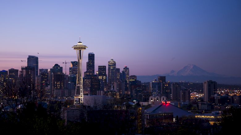The image shows the Seattle skyline at dusk, featuring the Space Needle with a mountain in the background.
