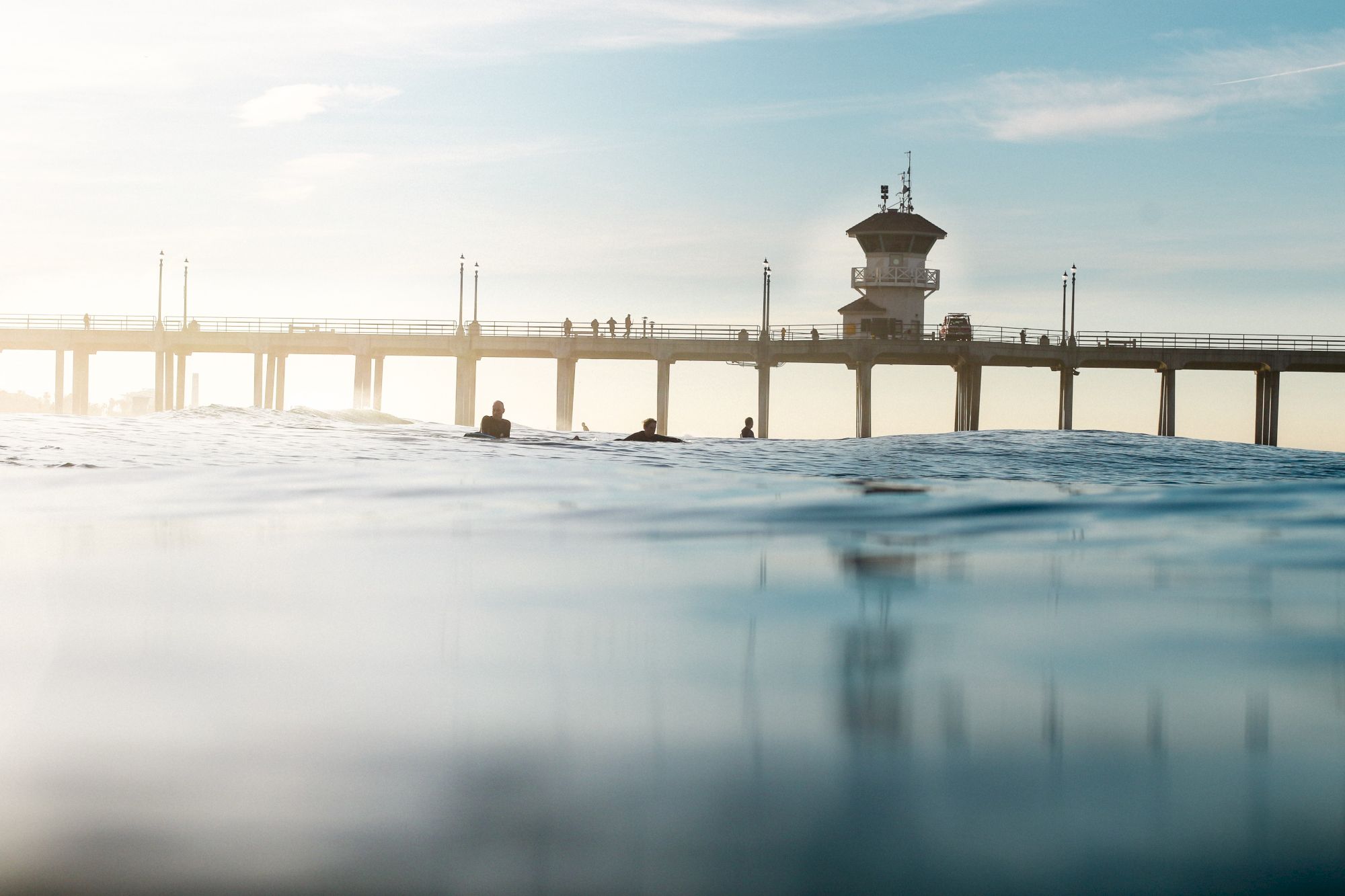 An ocean view with a pier stretching across the horizon and people walking on it, under a partly cloudy sky.
